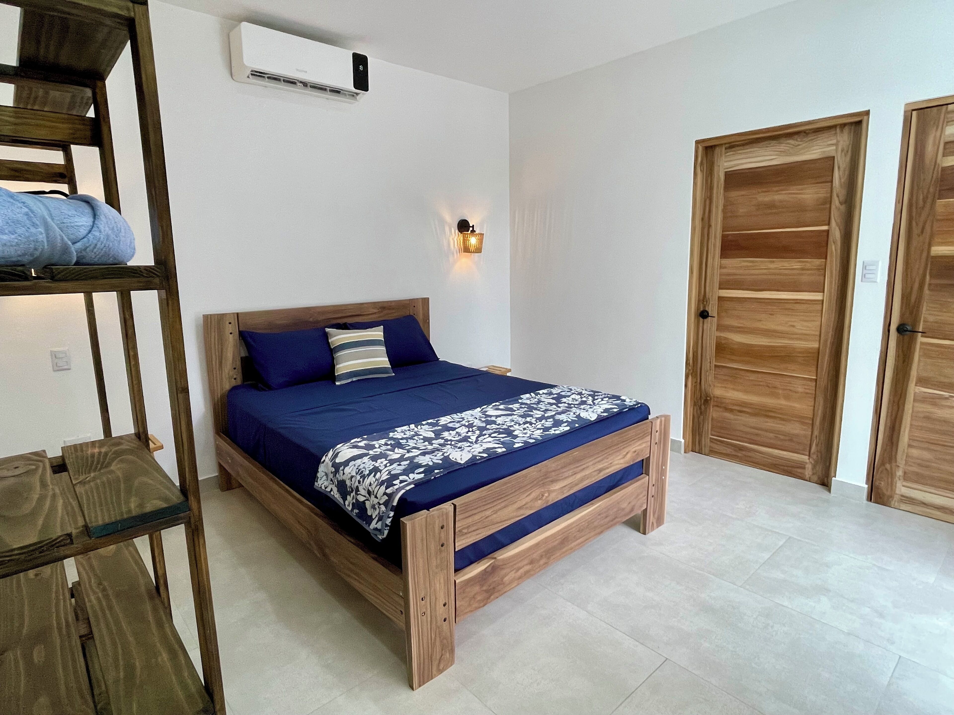 Ein Schlafzimmer mit einem hölzernen Bett, einem Nachttisch, einem Kleiderschrank und einer Wand-Klimaanlage.