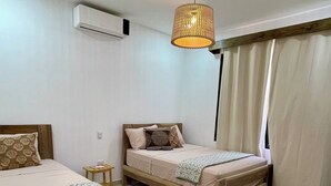 A bedroom with two beds, a small bedside table, a hanging light fixture, and a window with curtains. - Casa Solaz-Up to 7 people, parking and private pool-Playa Negra, Puerto Viejo (Puerto Viejo de Talamanca)