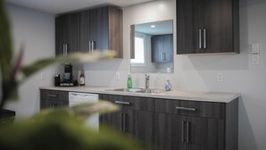 A modern kitchen with dark wood cabinets, a stainless steel sink, and a built-in oven. - Warm and Welcoming Basement (Dieppe)