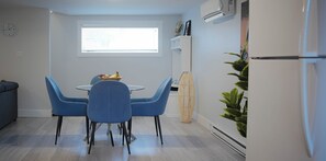 A modern kitchen with a dining table, blue chairs, a fruit basket, and a window.