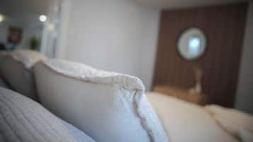 A close-up of a bed with white bedding, a wooden headboard, and a round mirror on a wooden nightstand.