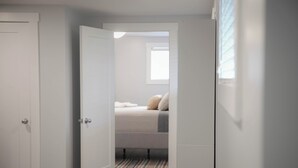 A bedroom with a bed, a window, and a door leading to another room. - Warm and Welcoming Basement (Dieppe)
