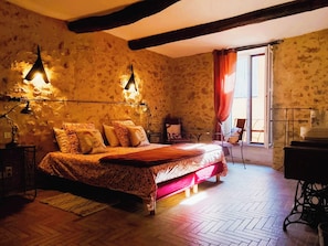 Une chambre à coucher avec un grand lit, deux lampes de chevet, un plancher en bois, une fenêtre avec des rideaux et une machine à coudre.