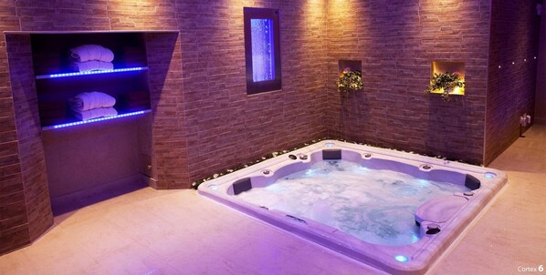 Une salle de spa équipée d’un bain à remous, d’un porte-serviettes et d’une étagère murale où sont rangées les serviettes.