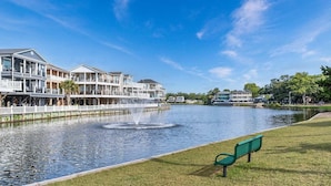 A waterfront property with a fountain, a grassy area with a bench, and a row of multi-story buildings. - 1009 Stunning 4Bed 4.5 Bath | Lake & Ocean Views (Myrtle Beach)