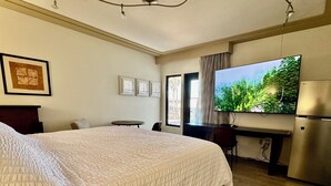 Ein Hotelzimmer mit einem großen Bett, einem Schreibtisch, einem Flachbildfernseher, einem Kühlschrank und einem Fenster mit Vorhängen.
