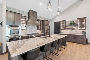 A modern kitchen with a large island, stainless steel appliances, dark wood cabinets, and a stone backsplash.