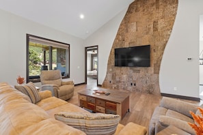 Un salon moderne avec un grand canapé d’angle, une table basse en bois et un téléviseur à écran plat fixé au mur.