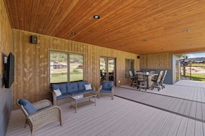 A covered outdoor area with wooden flooring, wicker furniture, and a dining table.