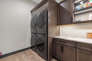 A laundry area with two stacked front-loading washers and dryers, wooden cabinets, and a marble countertop.