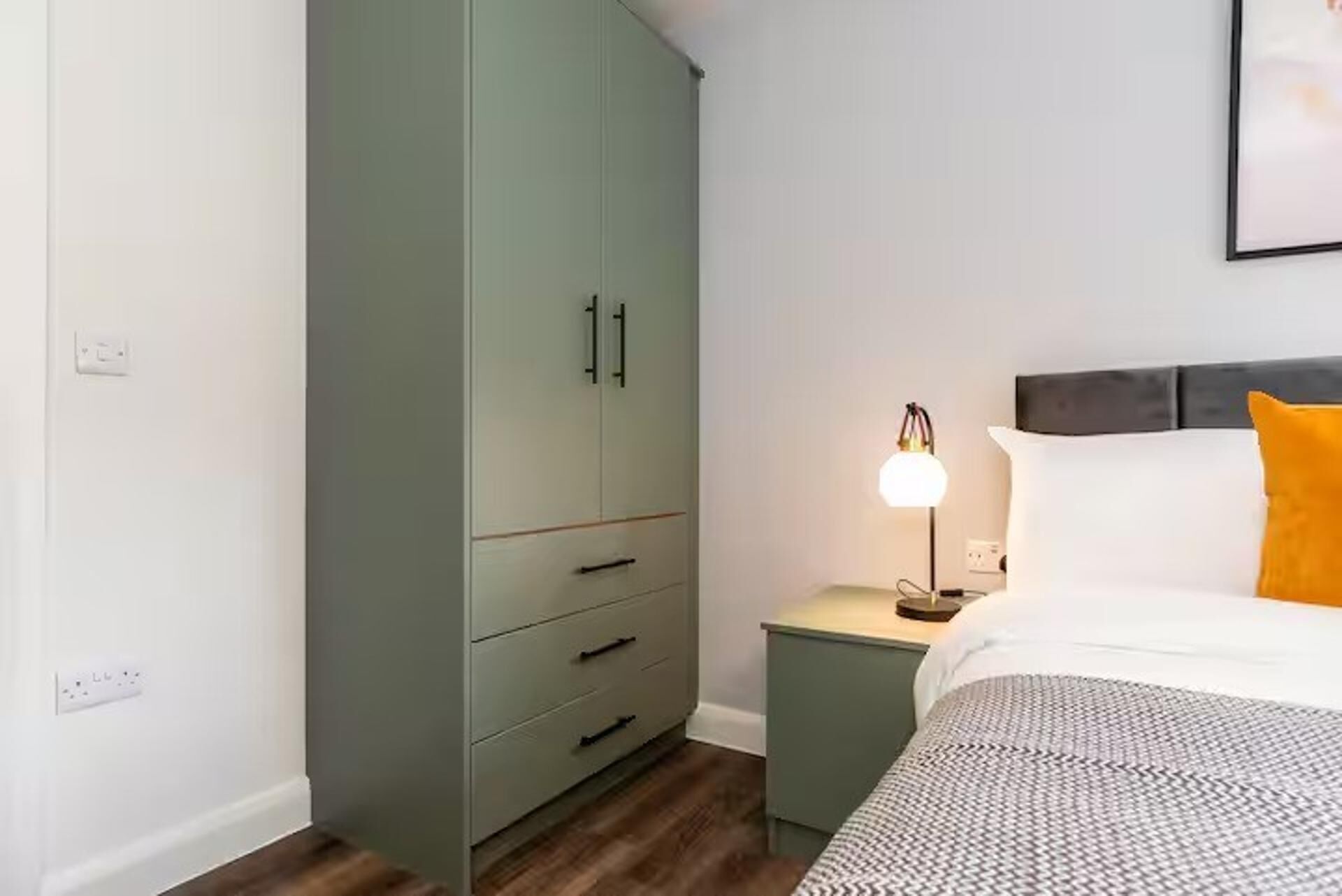 Et soveværelse med seng, natbord, lampe og garderobeskab.
