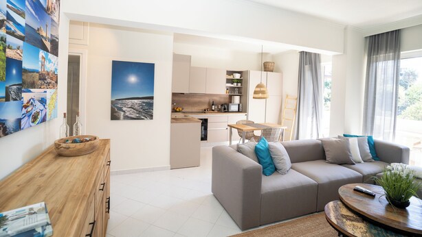 A modern living room with a grey sofa, wooden coffee table, and a kitchen in the background. - Design-Apartment mit 2 Balkonen & gehobener Ausstattung (Rodos)