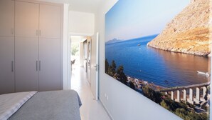 A bedroom with a large bed, a wardrobe, and a wall-mounted painting of a coastal scene. - Design-Apartment mit 2 Balkonen & gehobener Ausstattung (Rodos)