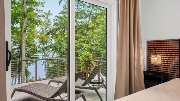 Ein Schlafzimmer mit Balkon, einem Bett, einem Nachttisch und einer Lampe.