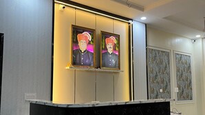 Un mostrador de recepción con detalles de mármol y negro, dos retratos enmarcados encima y papel tapiz estampado en las paredes.