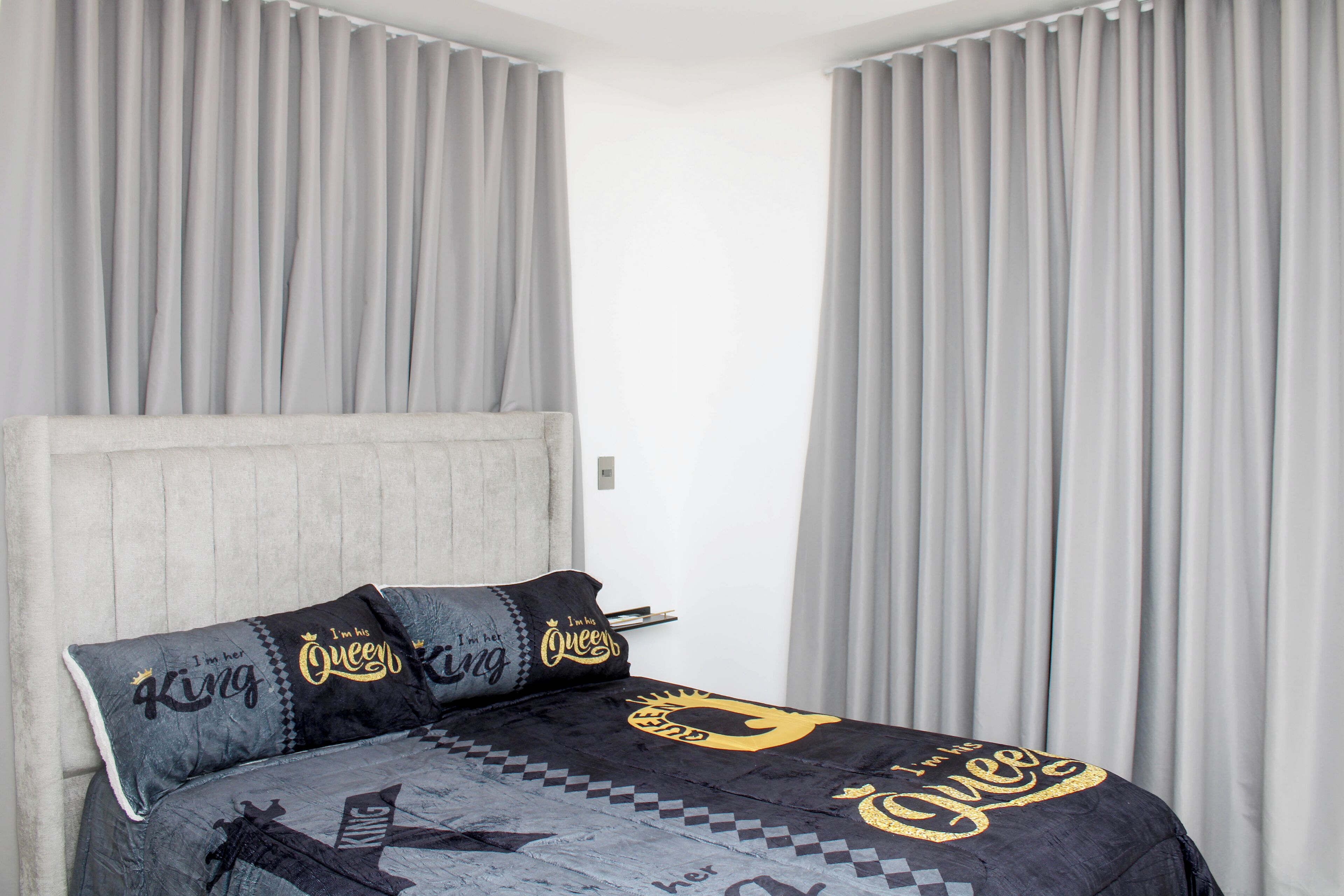 A bed with a grey headboard, grey curtains, and a black and grey bedspread with 'Queen' and 'King' text.