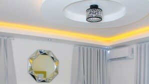 Un dormitorio moderno con una cama grande, un espejo decorativo, un equipo de aire acondicionado y una lámpara de techo.