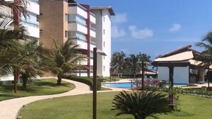 A resort with a pool, palm trees, and a building with balconies. - Costa Blanca #304 - Beachfront Apto by Carpediem (Aquiraz)