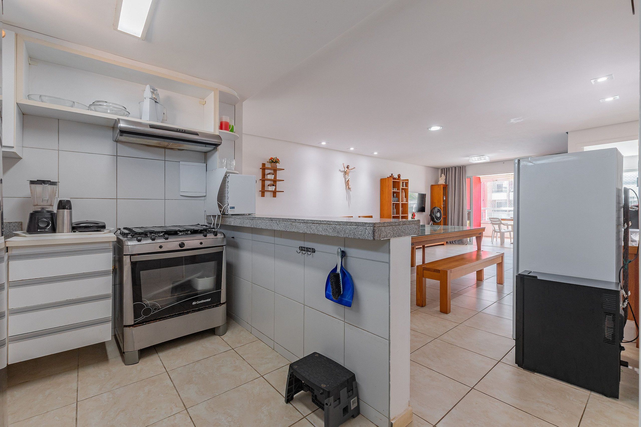 Una cocina moderna con estufa a gas, horno y microondas integrado. Hay un taburete y un banco en la zona de comedor.