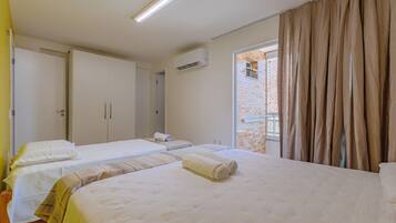 Una habitación de hotel con dos camas, una ventana con cortinas, un equipo de aire acondicionado y una puerta.