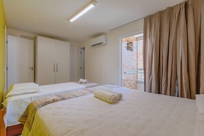 Une chambre d’hôtel avec deux lits, une fenêtre avec des rideaux, un appareil de climatisation et une porte.