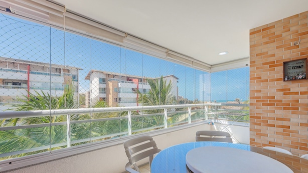 A balcony with a glass partition, a round table, and two chairs. - Costa Blanca #304 - Beachfront Apto by Carpediem (Aquiraz)