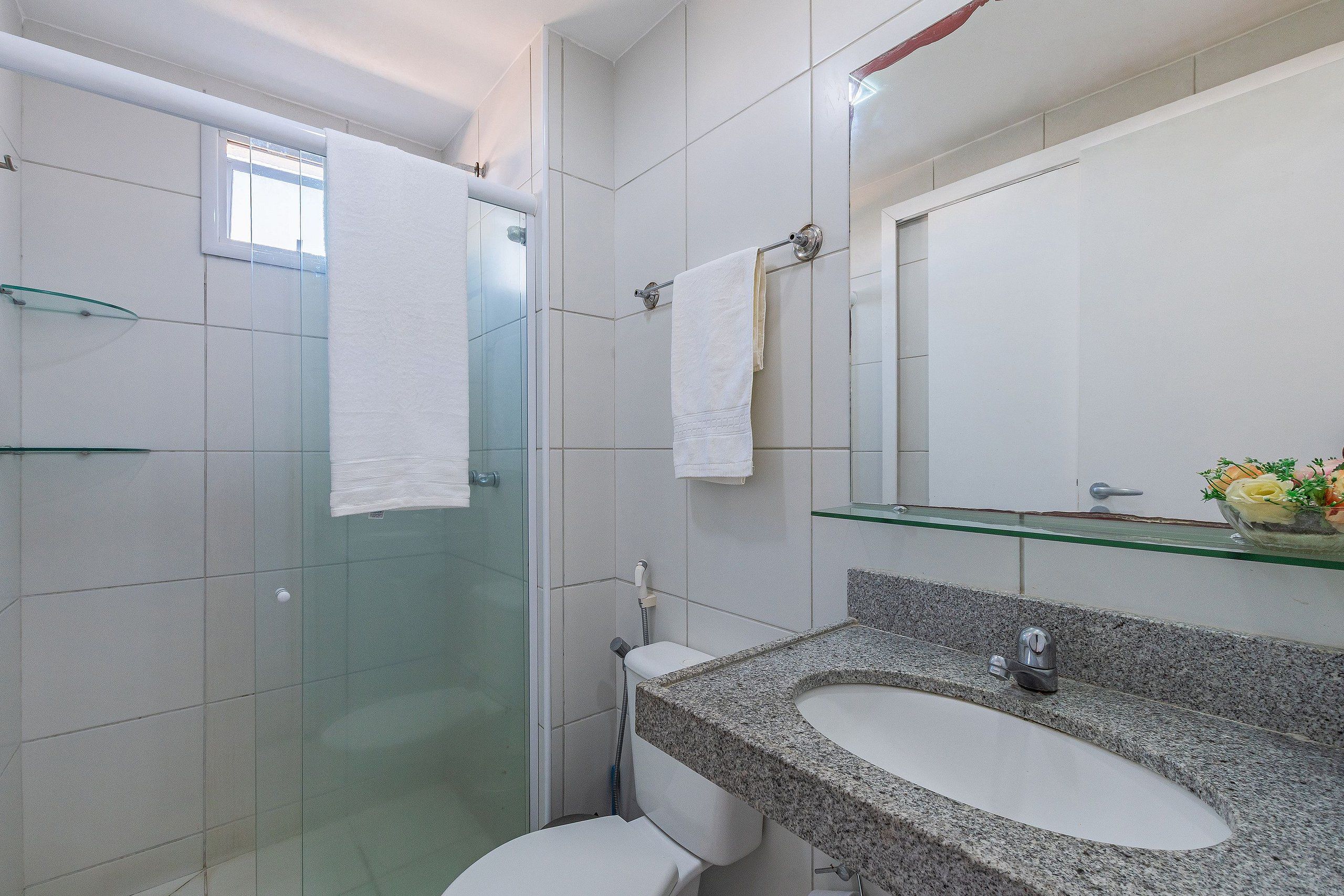 A modern bathroom with a glass shower enclosure, a white toilet, a granite sink, and a glass shelf above the sink.