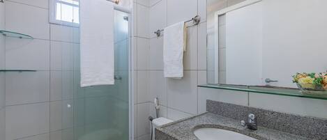 Un baño moderno con cabina de ducha de vidrio, inodoro blanco, lavamanos de granito y repisa de vidrio sobre el lavamanos.