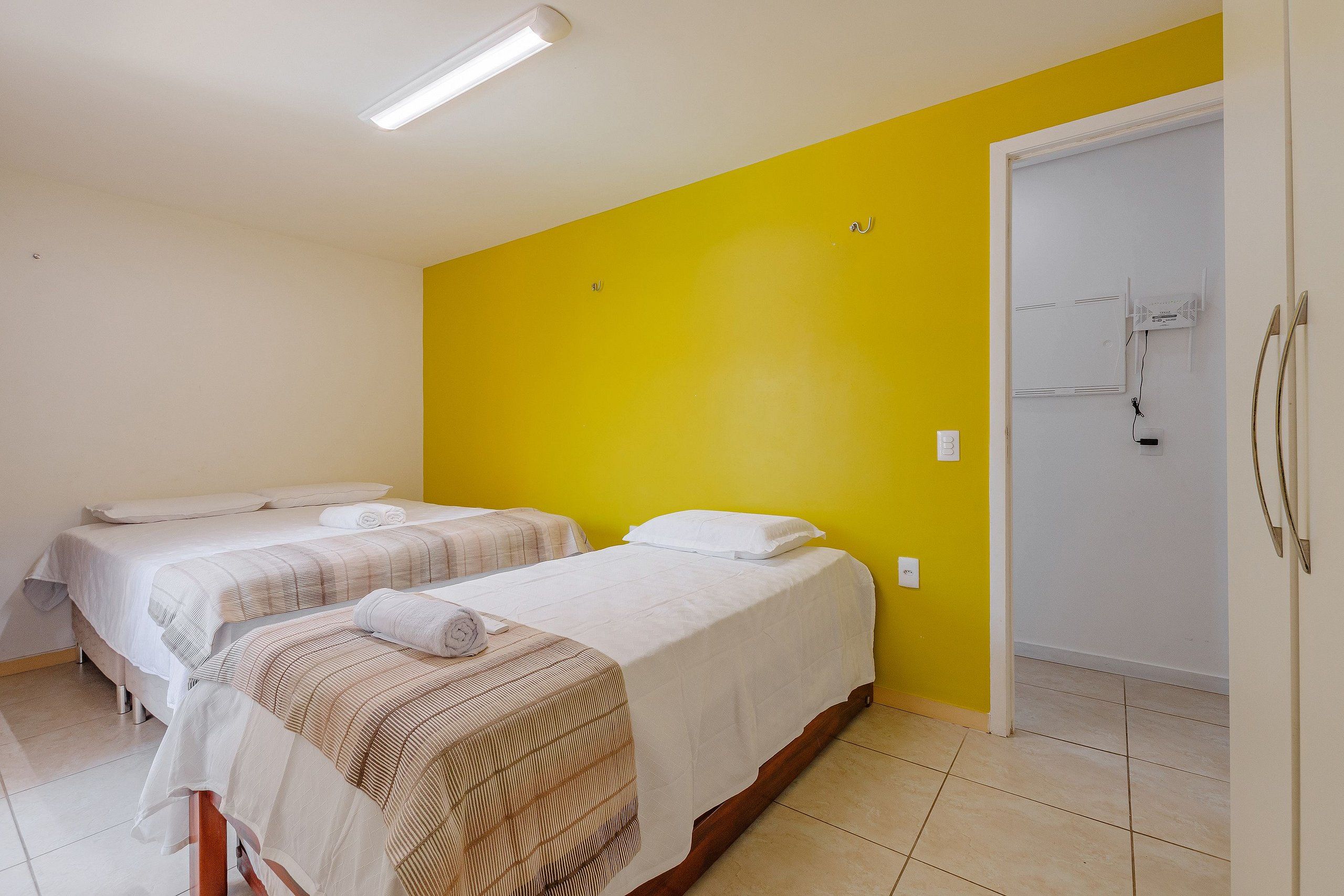 Ein Hotelzimmer mit zwei Betten, einer leuchtend gelben Akzentwand und einer weißen Tür.
