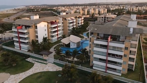 A coastal residential area with multi-story buildings, a swimming pool, and a beach in the background. - Costa Blanca #304 - Beachfront Apto by Carpediem (Aquiraz)