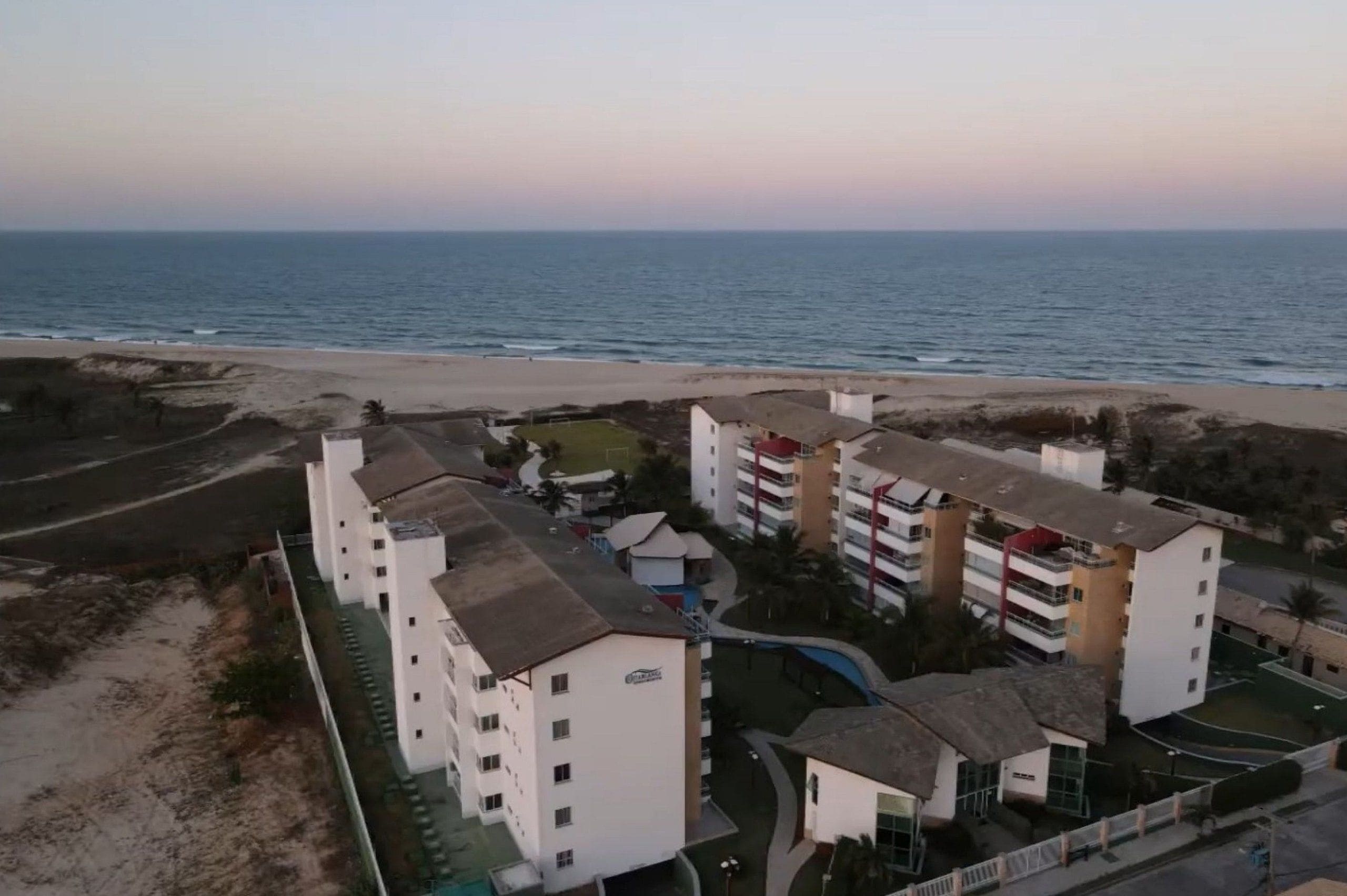Un hotel costero con varios edificios blancos, una playa al fondo y cielo despejado.