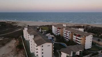 Un hotel costero con varios edificios blancos, una playa al fondo y cielo despejado.