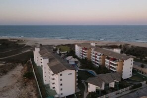 Un hôtel situé sur la côte, composé de plusieurs bâtiments blancs, avec une plage en arrière-plan et un ciel dégagé.