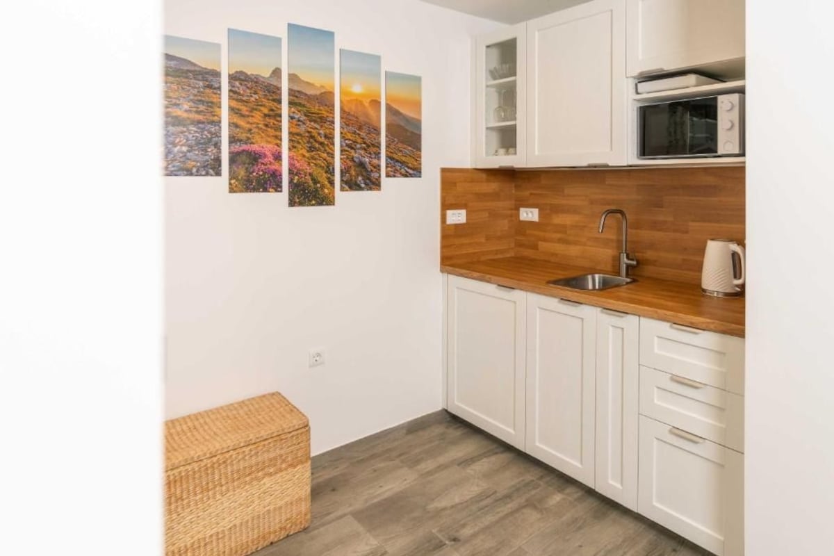A kitchenette with white cabinets, a wooden countertop, a stainless steel sink, and a microwave.