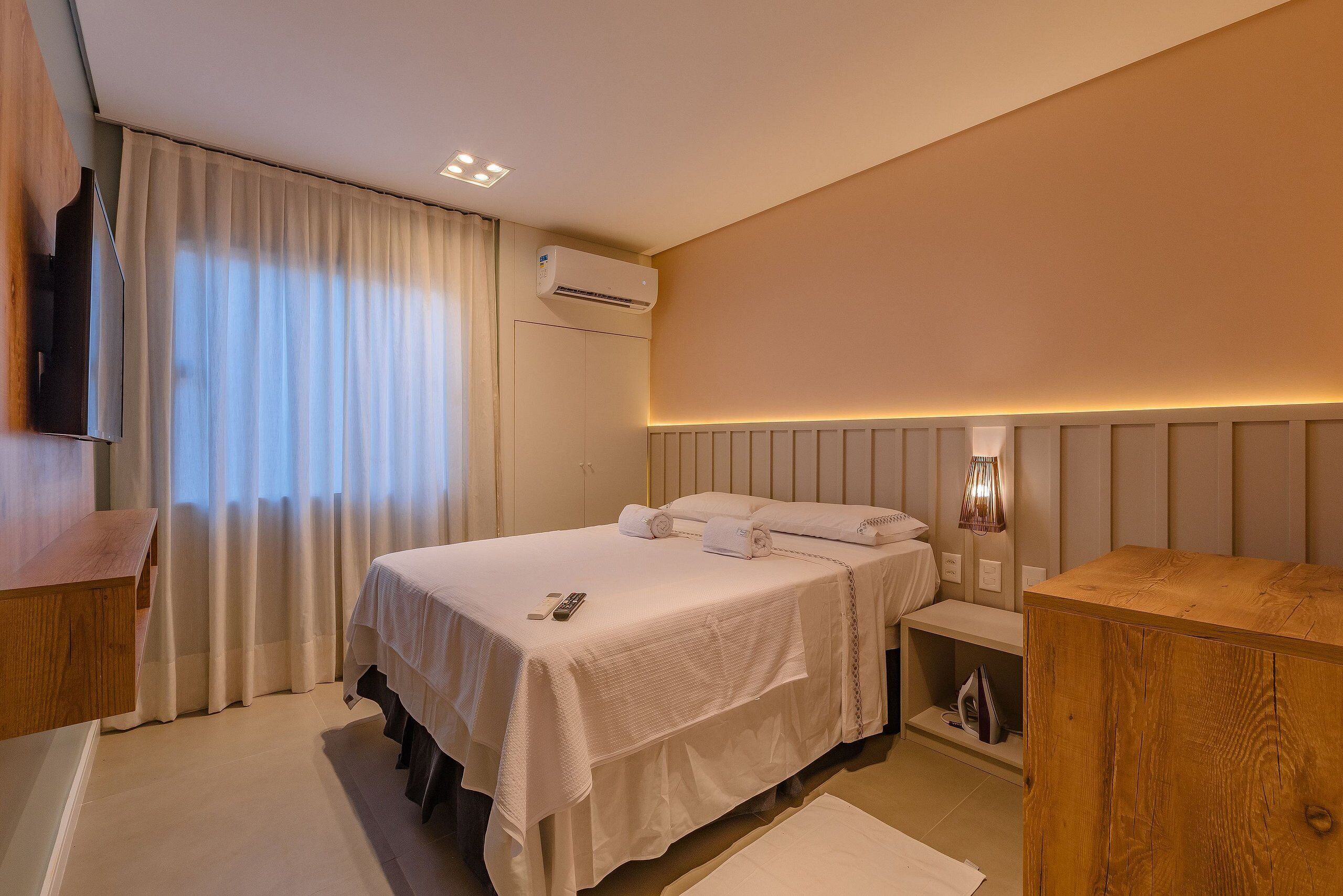 Una habitación de hotel con una cama, mesita de noche y televisión montada en la pared.