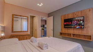 A hotel room with a large bed, a wooden headboard, a wall-mounted TV displaying Netflix, and a mirror above the bed. - Crystal Park #206 - Quadruplo por Carpediem (Aquiraz)