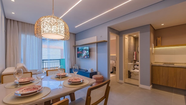 A modern dining area with a table set for four, a hanging light fixture, and a television mounted on the wall. - Crystal Park #206 - Quadruplo por Carpediem (Aquiraz)
