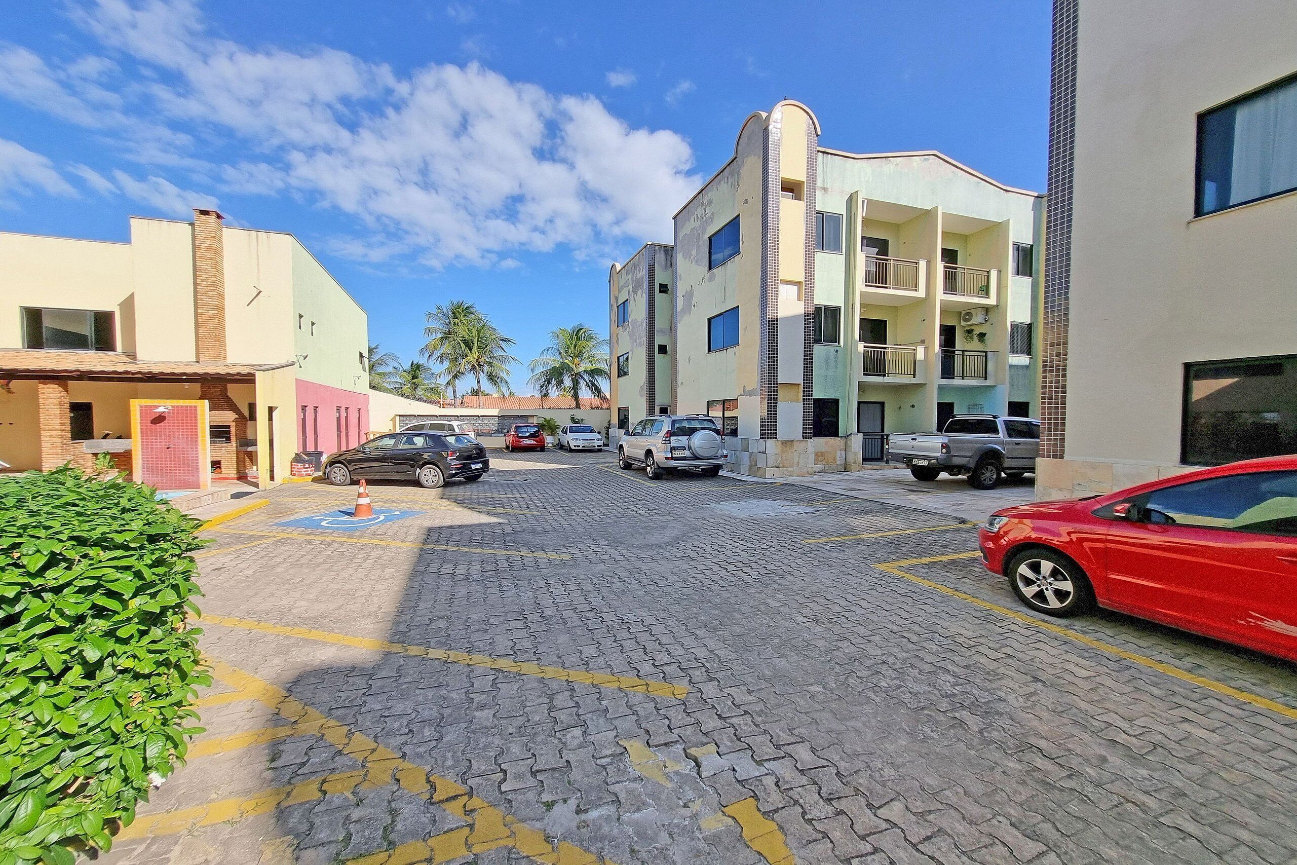 A parking area with multiple cars, a building with balconies, and palm trees in the background.