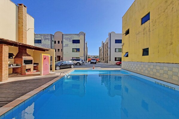 A swimming pool with a wooden deck, surrounded by buildings with balconies and windows.