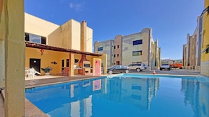 A swimming pool with a clear blue water surface, surrounded by buildings with a yellow facade and a red door. - Crystal Park #206 - Quadruplo por Carpediem (Aquiraz)