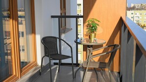 Een balkon met twee rieten stoelen, een klein rond tafeltje, een potplant en twee bekers.
