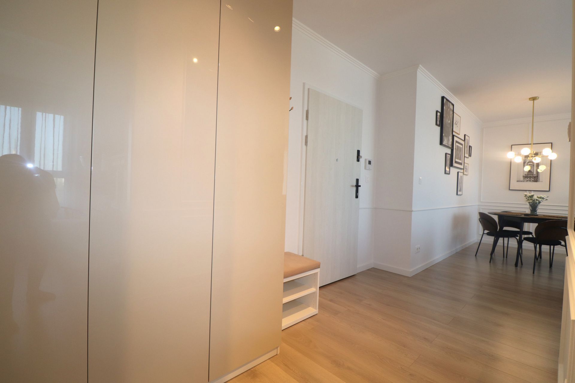 A modern interior with a wooden floor, a white door, a bench, and a dining area with chairs and a table.