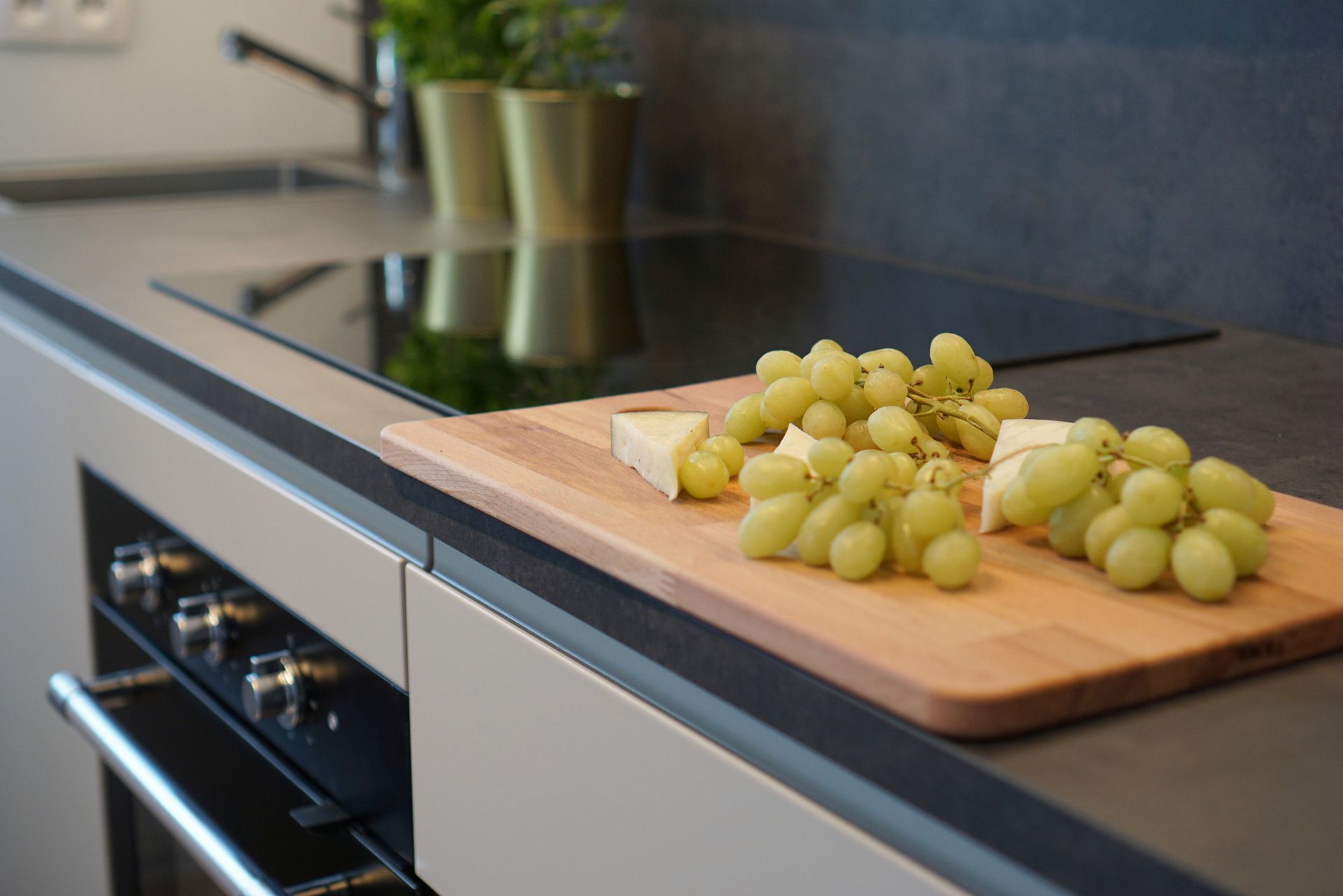 A kitchen counter with a cutting board, cheese, and grapes.