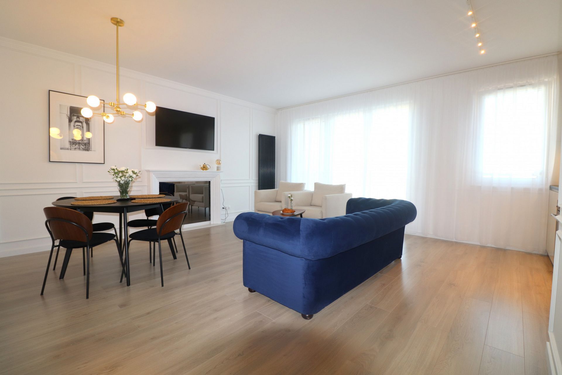 Una sala de estar moderna con un sofá azul, una mesa de comedor con sillas, una chimenea y un televisor montado en la pared.