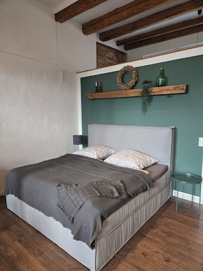 A bedroom with a bed, a nightstand, a wall-mounted shelf with decorative items, and a small table. - Old barn in the Nemitzer Heide (Trebel)