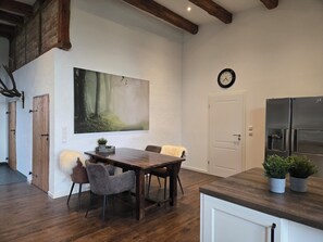 A modern kitchen with a wooden table and chairs, a large painting of a forest, a clock, and a refrigerator. - Old barn in the Nemitzer Heide (Trebel)