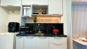 Een compacte keuken met een koffieapparaat, een waterkoker, een rode pan en een glazen wijnrek.