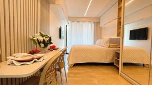 Een hotelkamer met een bed, een nachtkastje met een bloemetjesvaas, een stoel en een spiegel.