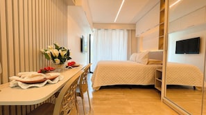 Habitación de hotel con una cama, una mesita de noche con un jarrón de flores, una silla y un espejo.