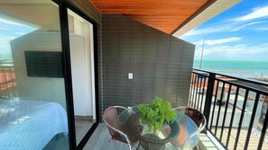 A balcony with a glass table, wicker chairs, and a potted plant. - OCEAN - STUDIO COM VARANDA - By Living (João Pessoa)